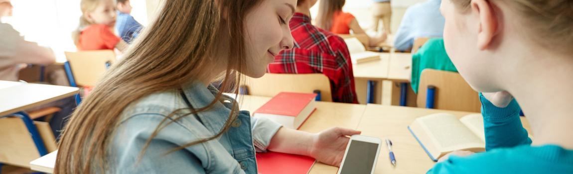 Fotolia/ Syda Productions zwei Mädchen sitzen an einer Schulbank und schauen auf ein Smartphone