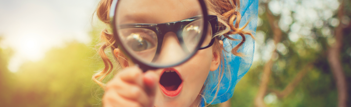 iStock.com/ ArtMarie Mädchen mit Kescher schaut mit großen Augen durch Lupe